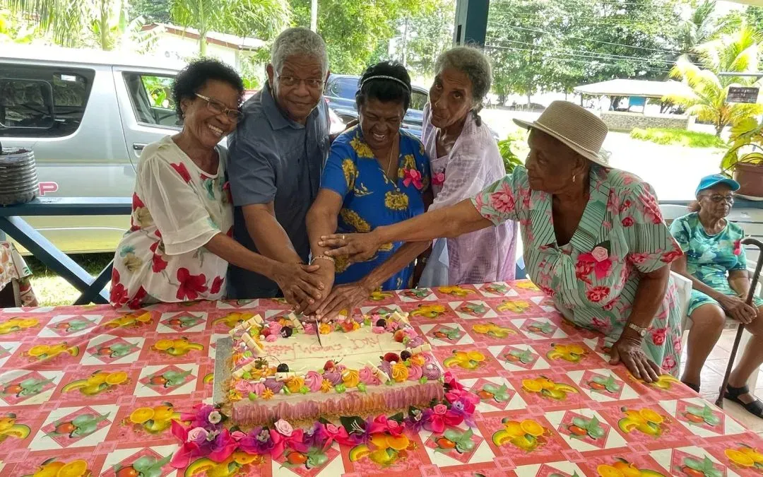 Elderly residents and the president cutting a decorated cake together during a celebration at Anse Boileau Elderly Home.