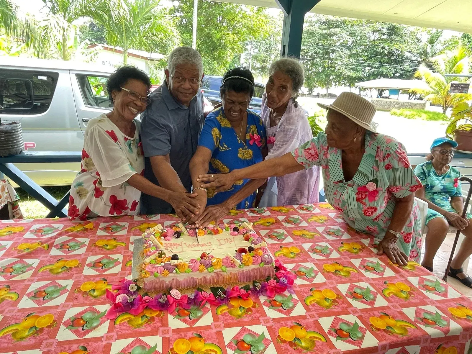 Elderly residents and the president cutting a decorated cake together during a celebration at Anse Boileau Elderly Home.